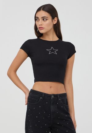 Cropped top nero a coste con maniche corte, caratterizzato da un design a stelle con borchie argentate sul petto. Abbinato a jeans neri a vita alta con dettagli.