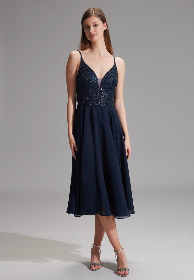 Robe bleu marine avec un corsage ajusté orné de sequins, décolleté en V profond et jupe fluide ; fines bretelles ajustables.