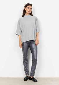 Szary, prążkowany, luźny top z wysokim kołnierzem, zestawiony z błyszczącymi, szarymi spodniami slim-fit i czarnymi mokasynami. Gładka tekstura na całej powierzchni.