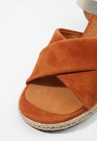 Sandale en daim marron avec design croisé, bout ouvert et semelle en jute tissé. Doublure intérieure lisse et dessus texturé pour le confort.