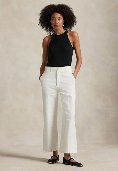 Czarny prążkowany top na ramiączkach w połączeniu z białymi spodniami o szerokich nogawkach. Spodnie mają przednie kieszenie i gładką fakturę. Czarne buty z ozdobnym przeszyciem.