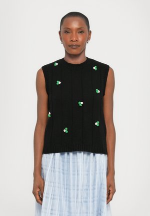 Zwarte gebreide mouwloze top met ribbelstructuur, versierd met kleurrijke geborduurde bloemaccenten in groen en roze, gedragen over een lichtblauwe rok.