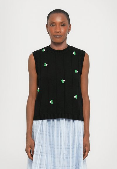 Haut sans manches en tricot noir avec une texture côtelée, arborant des accents floraux brodés colorés en vert et rose, porté sur une jupe bleu clair.