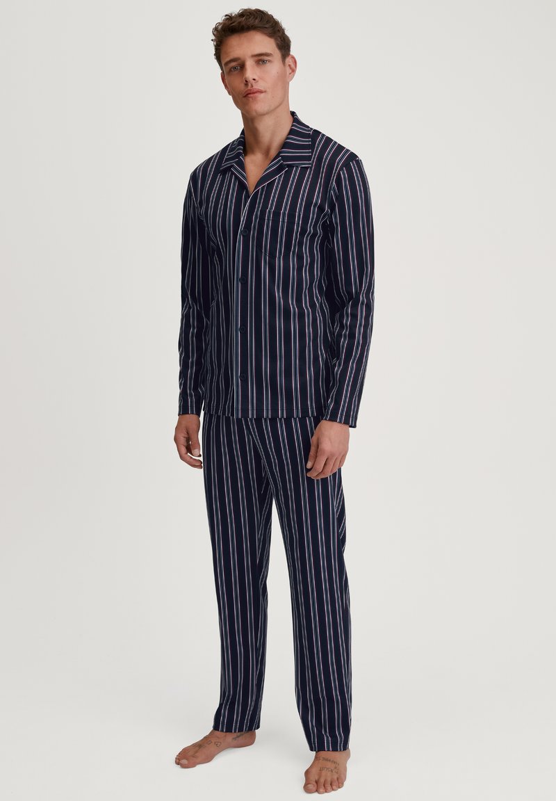 Marineblauwe gestreepte pyjama set met verticale rode en witte strepen, met een knoopsluiting shirt met een borstzak en bijpassende broek. Zacht materiaal, relaxed pasvorm.