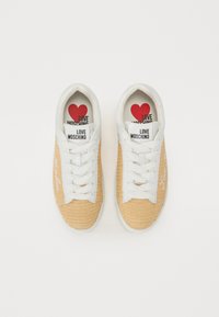Beige mesh sneakers with white leather accents, flat laces, and embossed logo on the side. Red heart with text on insoles.