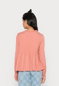 Camisola de mangas longas na cor pêssego, com decote drapeado, cintura franzida e bainha pregueada; combinada com calças xadrez de tom azul claro.