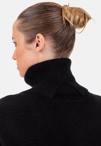 Pull noir à col roulé avec texture côtelée et col montant. Le tissu semble doux, avec un détail subtil à l'épaule. Cheveux coiffés en chignon.
