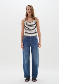 Randig svart- och vit t-shirt med V-hals, i kombination med lösa blå denimjeans och svarta slidesandaler. Enkel och avslappnad design.
