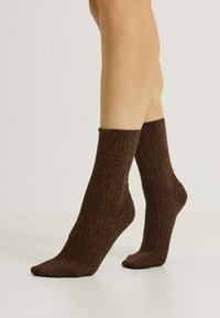 Calcetines marrones con relieve hechos de un material texturizado y brillante, que presentan una longitud hasta la mitad de la pantorrilla y un diseño de puño enrollado ceñido.