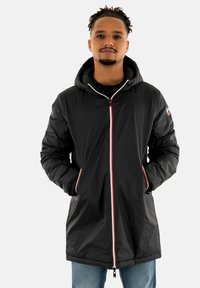 Veste à capuche noire avec une finition brillante, fermeture éclair à l'avant avec des accents rouges et blancs, poches latérales et une longueur légèrement plus longue.