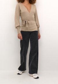 Beige wrap sweater with a deep V-neck, long puff sleeves, and a tie at the waist, paired with dark jeans and white sneakers.