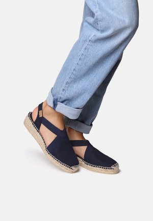 Ciemnoniebieskie espadryle z płócienną cholewką, elastycznymi krzyżującymi się paskami i jutyową podeszwą. But posiada przeszycie wzdłuż krawędzi.