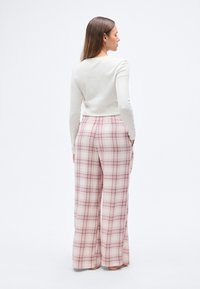 Κρεμ μπλούζα με μακριά μανίκια συνδυασμένη με φαρδιά καρό παντελόνια σε ανοιχτό ροζ και μπορντό. Το παντελόνι έχει ελαστική μέση και φαρδιά πόδια.