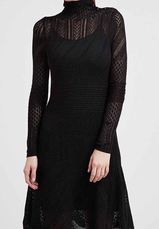 Robe noire en tricot avec manches longues, col montant, motifs texturés et jupe évasée. Présente des motifs de point complexes et une légère transparence.