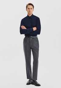 Granatowa koszula na guziki zestawiona z szarymi, dopasowanymi spodniami i czarnymi skórzanymi butami. Gładki materiał i dopasowany krój z bocznymi kieszeniami.