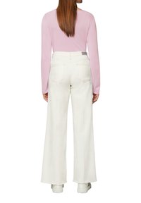 Białe szerokie spodnie z wysokim stanem i pięcioma kieszeniami, zestawione z długim rękawem jasnoróżowej bluzki. Gładki materiał z minimalnymi detalami szycia.