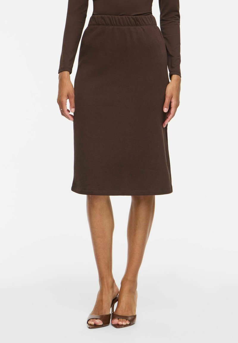 Femme portant une jupe marron longueur genou avec une ceinture élastique et un haut à manches longues assorti, associée à des talons ouverts marron.