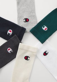 Seis pares de calcetines acanalados en azul marino, gris, verde, negro, blanco y crema, que presentan un logo con acentos rojos y negros en cada calcetín.