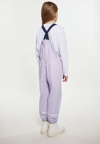 Lilac krāsas ūdensizturīgas virsdrēbes ar tumši zilām siksnām, elastīgu jostasvietu un atstarojošiem akcentiem pie piedurknēm. Valkātas virs garām piedurknēm baltas krekliņa.