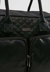 Black quilted synthetic leather bag featuring dual zippered front pockets, short handles, and a metal brand tag. Durable and textured surface.