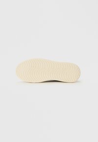 Light beige shoe sole with curved and parallel groove patterns for traction, shown against a plain white background.