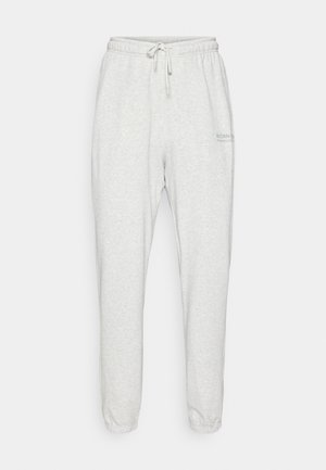 Pantaloni tuta grigi chiari con cintura elastica, cordino e orli a costine. Presentano un marchio discreto in verde sul lato sinistro.