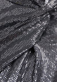 Tessuto nero decorato con paillettes argentate riflettenti, caratterizzato da un motivo testurizzato e intrecciato e un dettaglio annodato nella parte superiore.