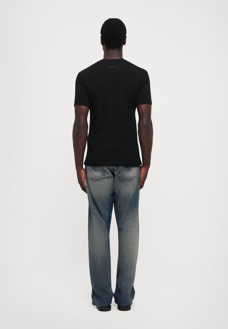 Sort bomulds t-shirt med korte ærmer, parret med løse, blegede blå denim jeans. Set fra ryggen mod en ensfarvet hvid baggrund.