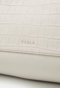 Borsa a mano in pelle beige con texture effetto coccodrillo e base liscia. Presenta il logo "FURLA" impresso a rilievo. Cuciture precise e finitura morbida.