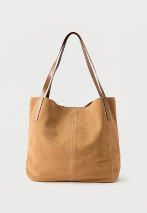 Sac fourre-tout en daim beige avec de longues anses en cuir marron clair, texture douce et couture simple sur un fond blanc uni.