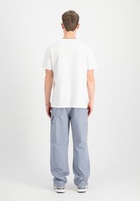 Camiseta blanca de manga corta combinada con pantalones cargo gris claro que cuentan con bolsillos laterales, corte holgado y material cómodo.
