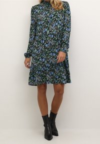 Robe florale noire, ornée de fleurs bleues et vertes, à manches longues, avec un col haut et un ourlet en cercle. Assortie à des bottines noires.