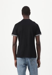 T-shirt preta de mangas curtas com riscas brancas nas bainhas. Feita de algodão, possui um decote redondo clássico e um corte confortável.