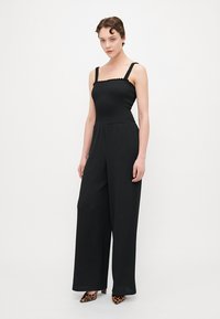 Zwarte jumpsuit met een aansluitend bovenlijfje, wijde pijpen, textuurstof en verstelbare bandjes. Gestyled met luipaardprint schoenen.