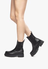 Botas de tobillo de cuero negro con paneles laterales elásticos, suela de goma resistente y tiradores. Textura suave y diseño robusto.