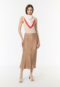 Beige ärmelloses Strickoberteil mit einem rot- und cremefarbenen gemusterten Schal; seidiger brauner Midirock; helle beige knöchelhohe Sandalen mit Absatz.