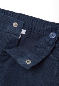 Donkerblauwe corduroy stof kenmerken, met een ribbelstructuur, een elastische tailleband en een metalen drukknoopsluiting naast een knopdetail.