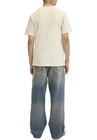 T-shirt crème à manches courtes associé à un jean décontracté, léger et déchiré. Le tissu semble doux, avec des coutures visibles et une coupe décontractée.