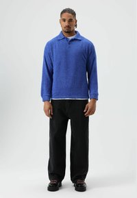 Zachte blauwe fleece trui met een kraag, gecombineerd met losse zwarte spijkerbroek en zwarte schoenen met roze veters. Over het geheel een gladde textuur.