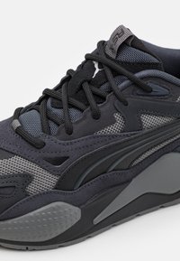 Baskets noires et grises en mesh et daim, design complexe, détails texturés, et semelle en caoutchouc épaisse.