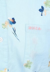 Lichtblauwe katoenen shirt met bloemenprint, voorzien van veelkleurige bloemen. Inclusief een borstzak met "N.Z.A." geborduurd in het roze.