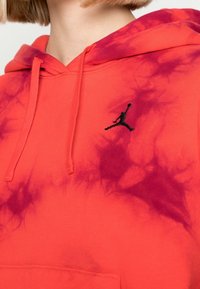 Rød hoodie med lilla tie-dye mønster, snøre i halsen og et sort broderet Jumpman-logo på brystet. Blødt bomuldsstof.