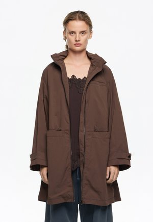 Chaqueta marrón oversized con cremallera y capucha, que cuenta con dos bolsillos delanteros y mangas anchas, hecha de una tela ligera y suave.