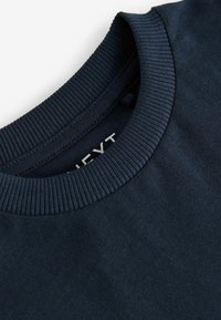 Felpa blu navy con colletto rotondo a coste, texture liscia e un piccolo etichetta con il nome del brand all'interno del collo.