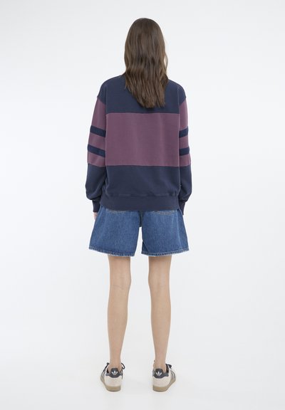 Hanorac cu blocuri de culoare bleumarin și vișinie, având dungi orizontale pe mâneci; asortat cu pantaloni scurți din denim și adidași.