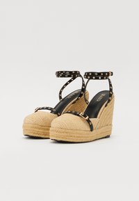 Sandalias de cuña espadrille negras con un tacón de yute trenzado, con detalles de tiras negras y tachuelas doradas. Forro interior suave con detalles del logo.