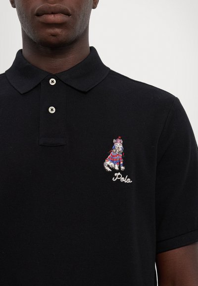 Cămașă polo neagră cu un design colorat brodat reprezentând un câine și textul "Polo" pe pieptul stâng, cu guler clasic și închidere cu două butoane.