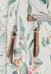 Sac à dos en simili cuir blanc à motif floral, avec des feuilles vertes et des fleurs colorées ; fermeture éclair argentée avec des tirettes en cuir beige.