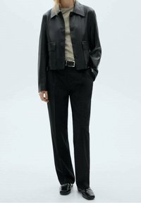 Veste en cuir noire avec un col à revers, une fermeture à boutons et des poches avant. Assortie à un pantalon noir taille haute et des chaussures noires.