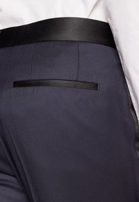 Pantaloni bleumarin cu o textură netedă, un tiv din satin negru și o singură buzunară din spate cu un detaliu de margine neagră.